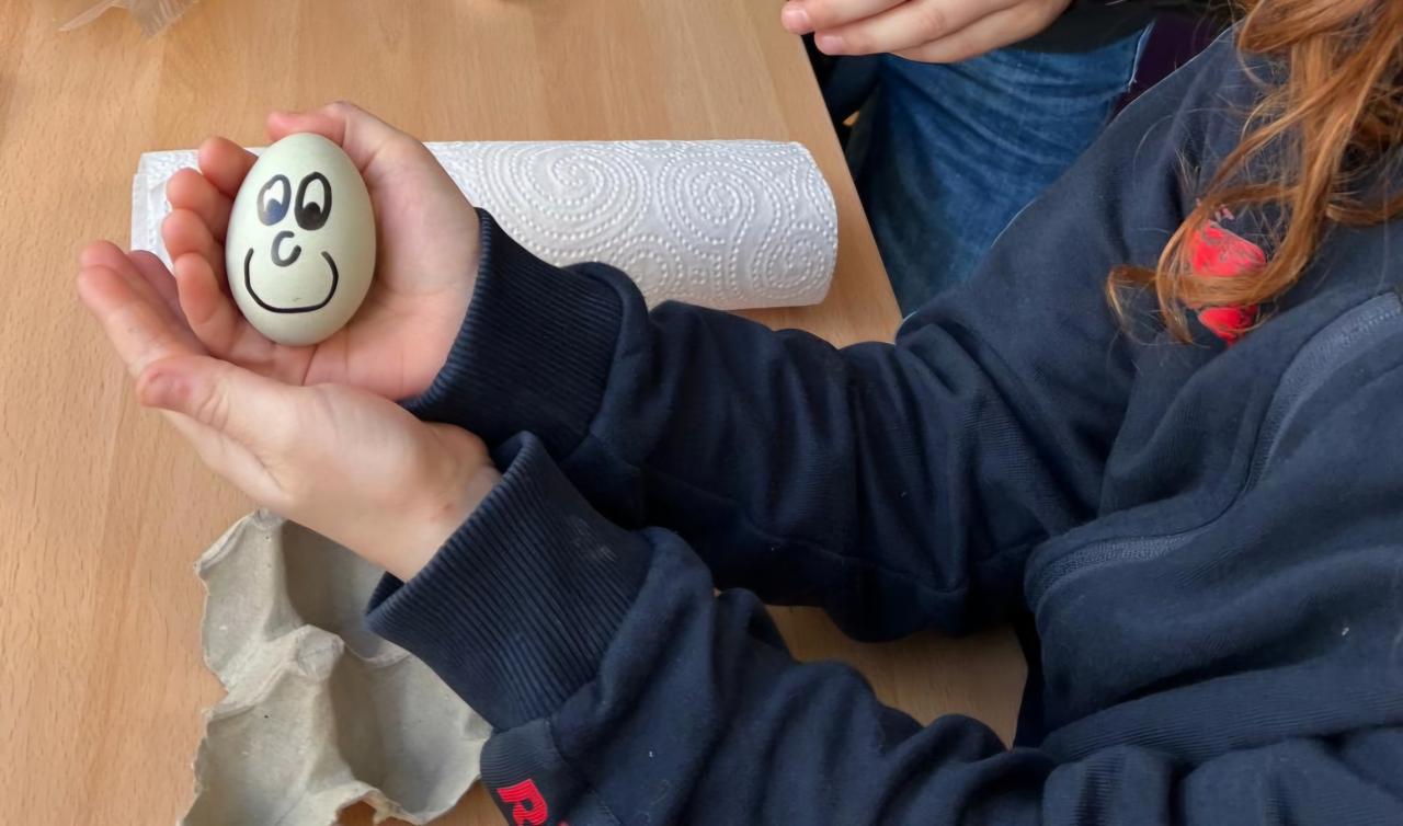 Ei mit bemaltem Gesicht in einer Kinderhand