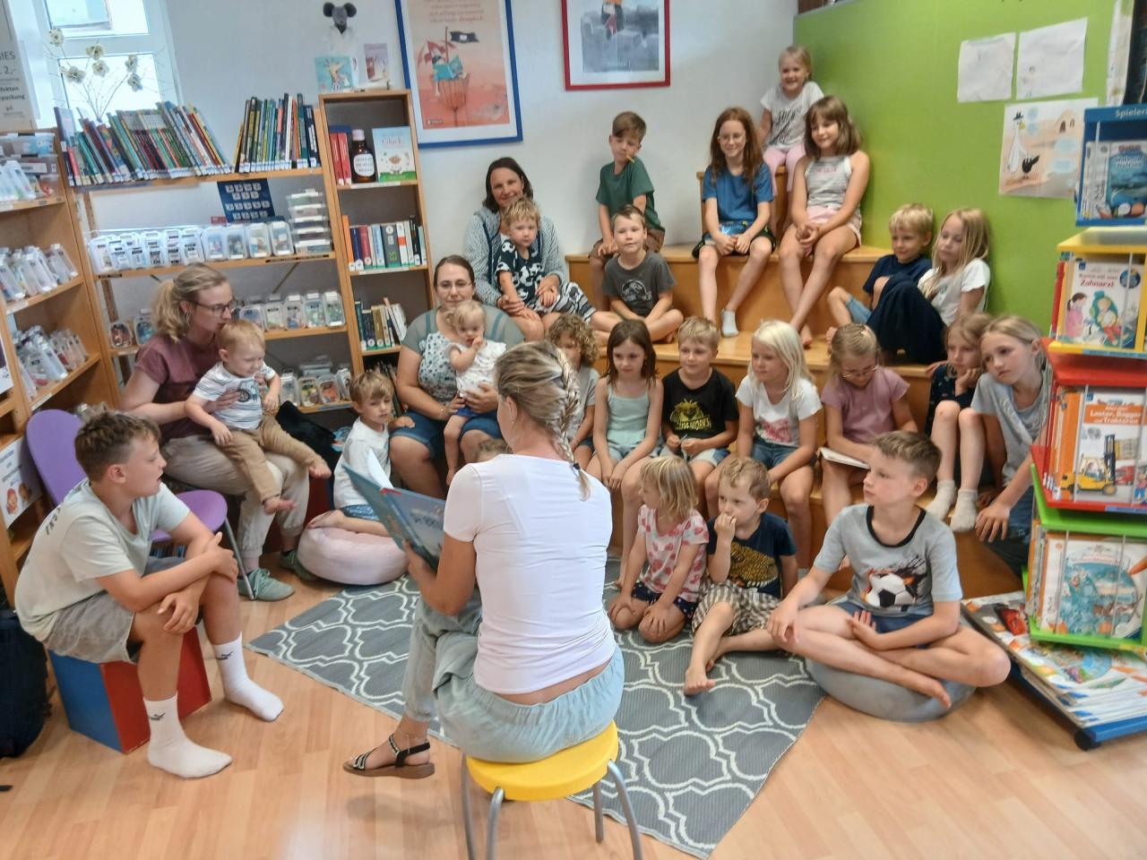 Kinder sitzen auf einer Sitztreppe und hören einer Frau zu